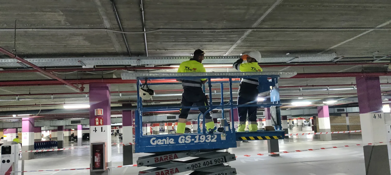 Dos técnicos de TLR sobre una plataforma elevadora montando luminarias en un aparcamiento